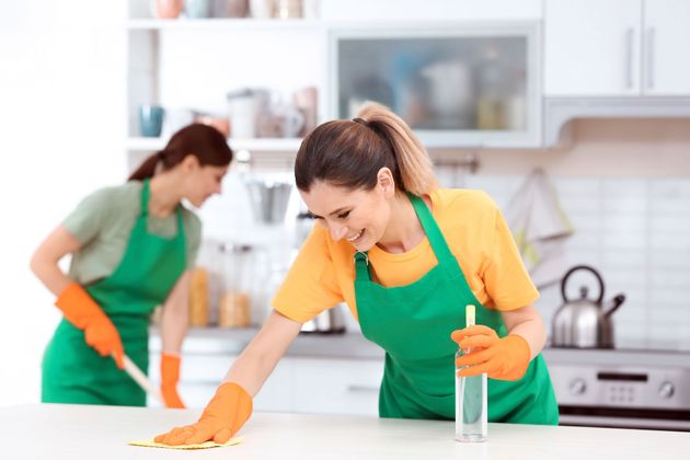 Two cleaners in green aprons wiping a bright kitchen countertop with cloths