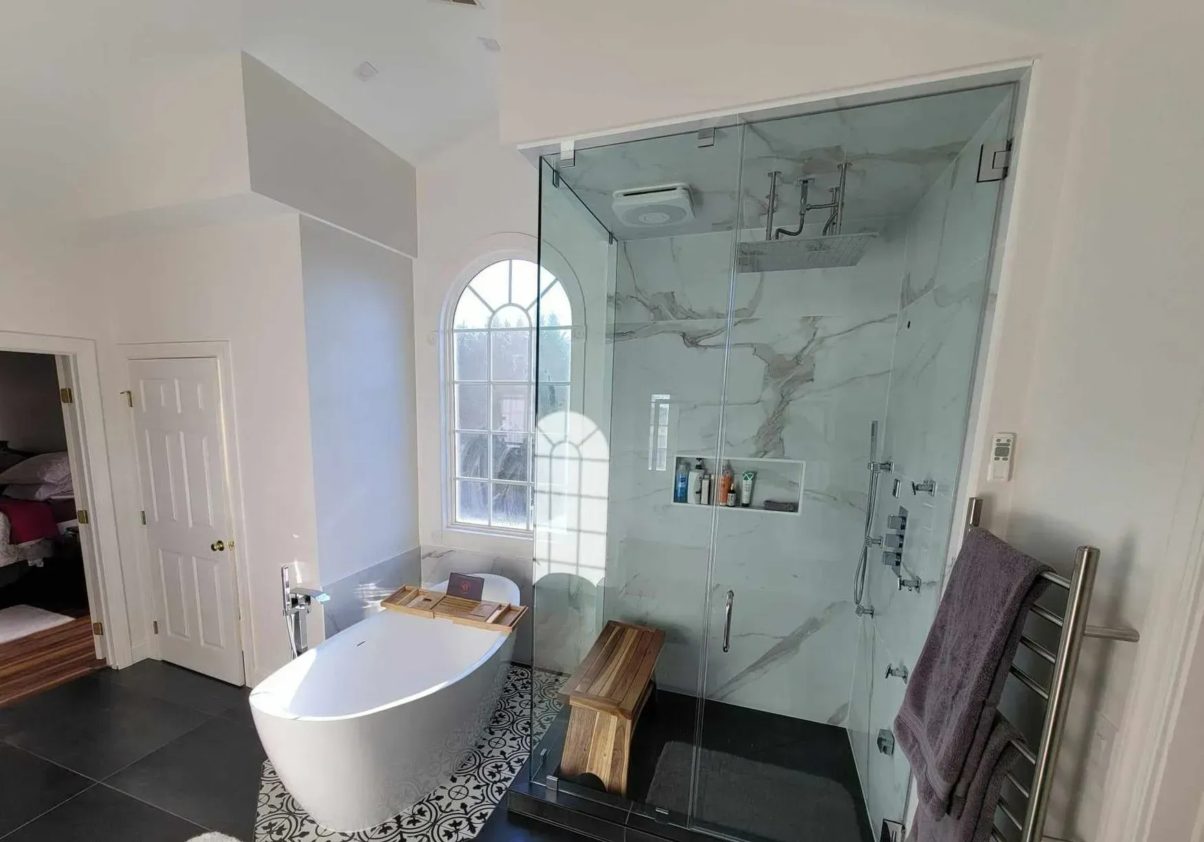 Bathroom with gray-tiled shower, white toilet, vanity, and a dark accent wall with a round mirror.