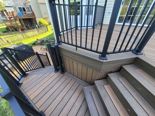A wooden deck with stairs leading down to a lower level, featuring black railings and a matching staircase design.