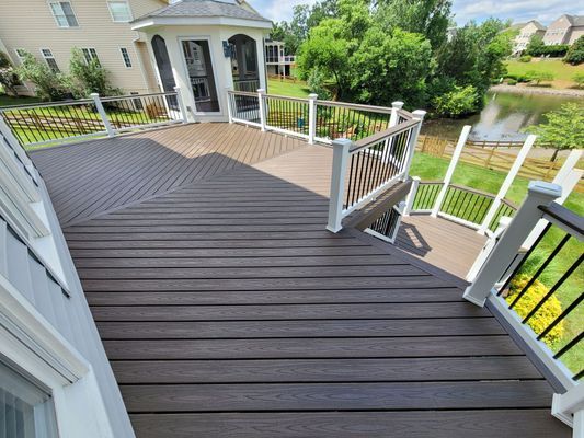 A multi-level dark brown composite deck with white railings, overlooking a backyard pond and surrounding greenery.