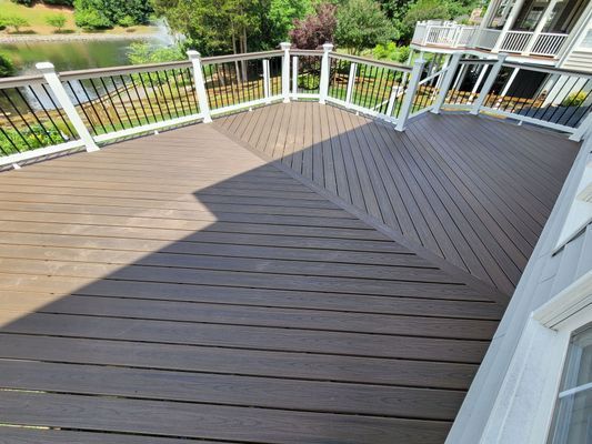 A high-angle view of a large, dark brown composite deck with diagonal patterns, white railings, and a lake in the background.