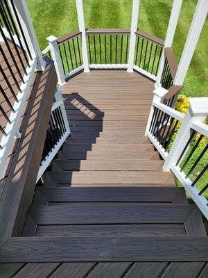 A view looking down a set of dark brown wooden deck stairs to a curved lower platform with white railings and grass.