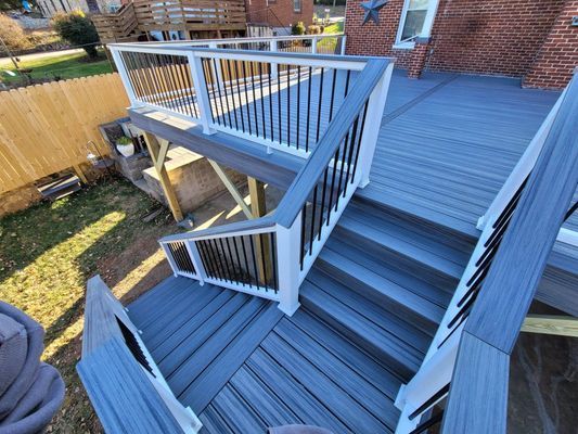 A high-angle view of a grey composite deck with white railings and black balusters, featuring stairs leading to the yard.