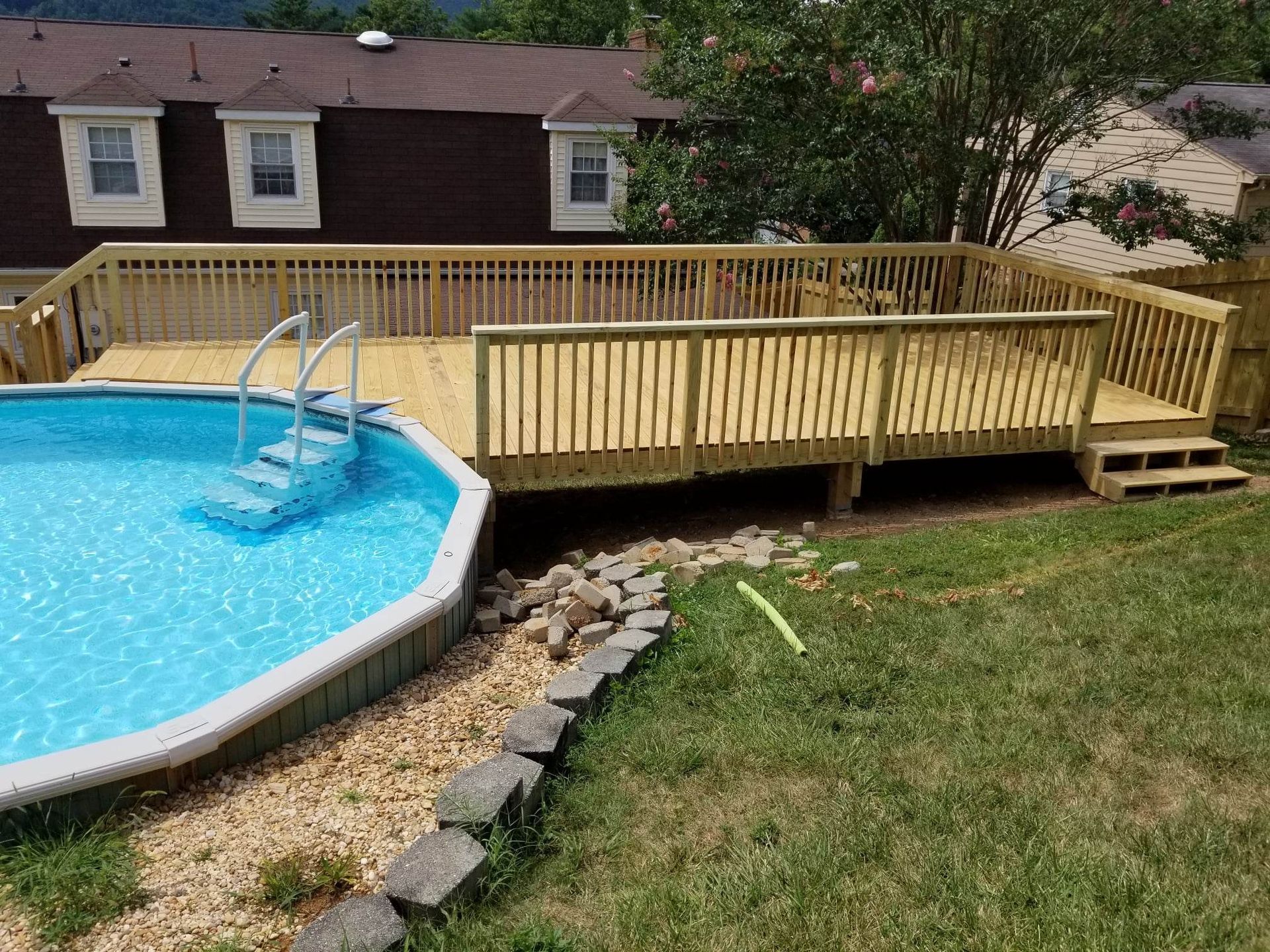 An elevated wooden deck with railings surrounding part of an above-ground swimming pool in a residential backyard.