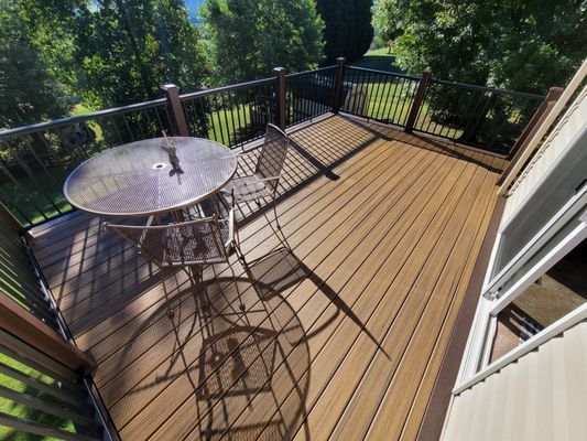 A deck with brown composite decking, a glass-top table, and chairs with a view of trees.