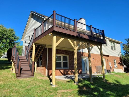 Two-story deck attached to a house with stairs and brown railings, supported by wooden posts.
