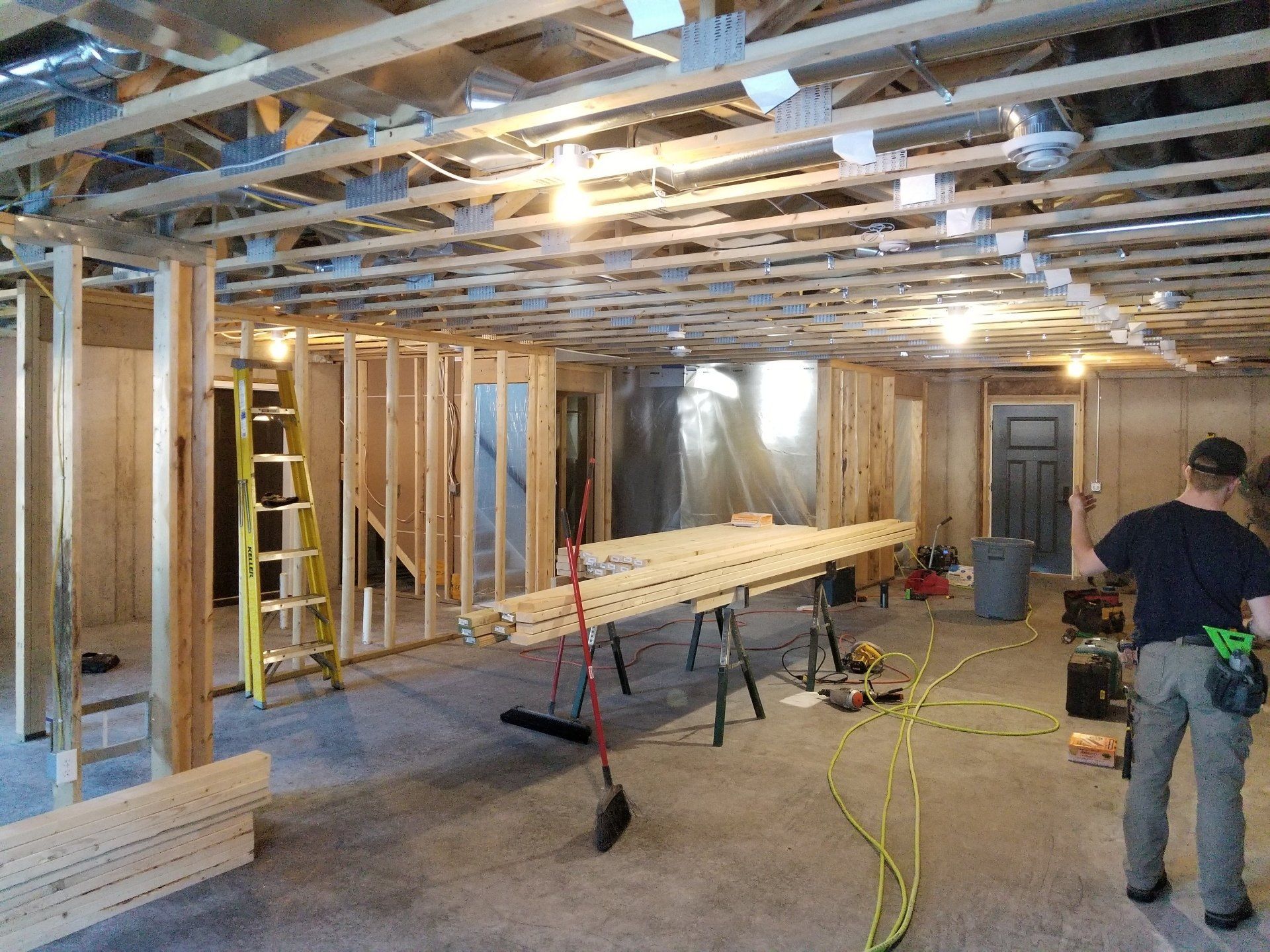 Basement under construction: wooden frames, exposed ceiling, tools, a worker, concrete floor.