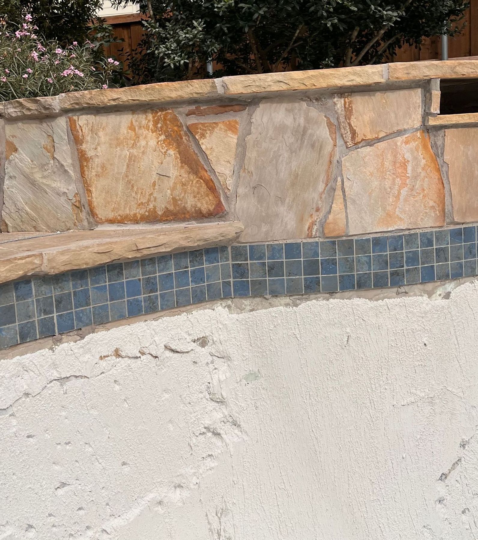 A stone wall surrounds a swimming pool with trees in the background.