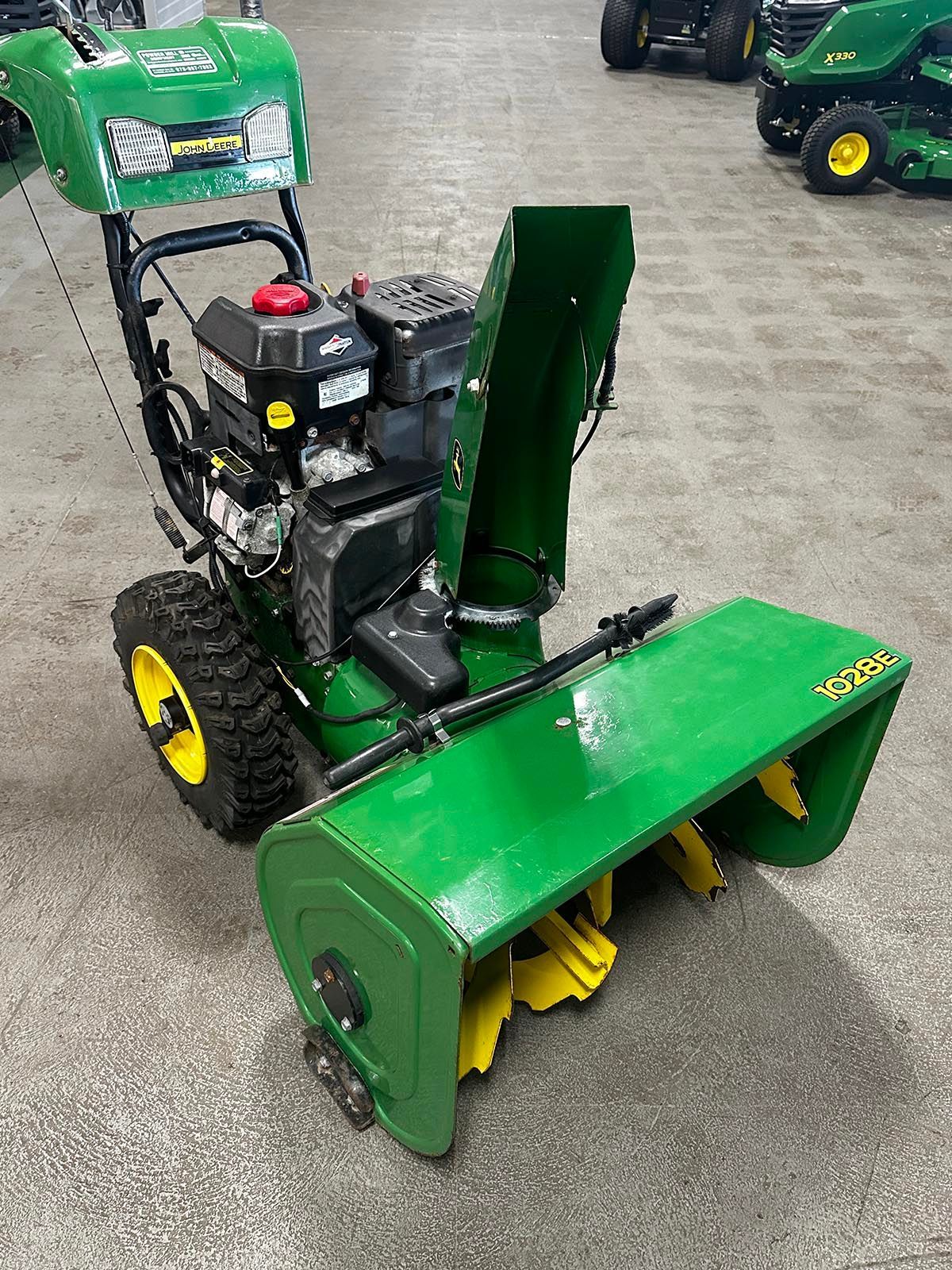 A green yellow snowblower is sitting on a concrete floor