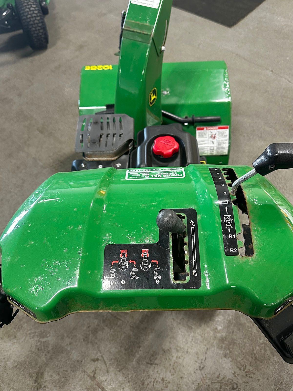 A green snowblower is sitting on a concrete floor