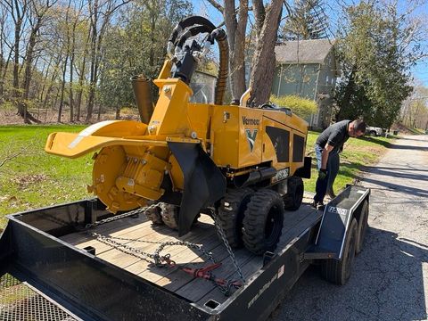 Yellow wood chipper loaded on a trailer, with a person standing beside it outdoors on a sunny day.