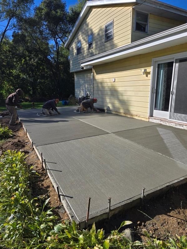 A concrete patio is being built in front of a yellow house.