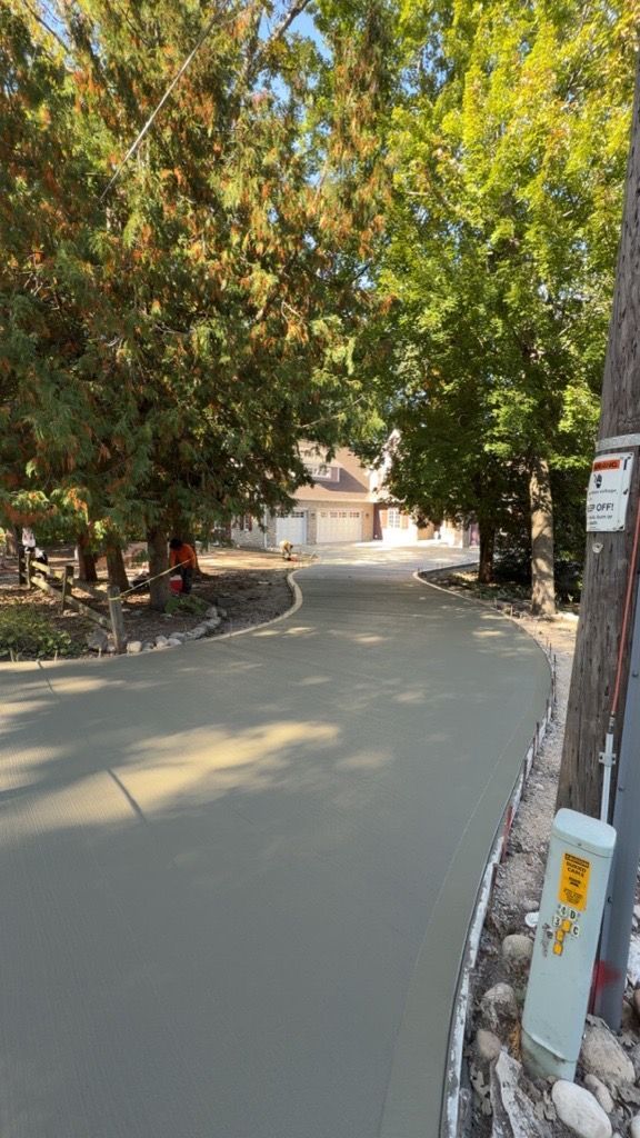 Newly paved residential street with trees, a house, and a utility pole.