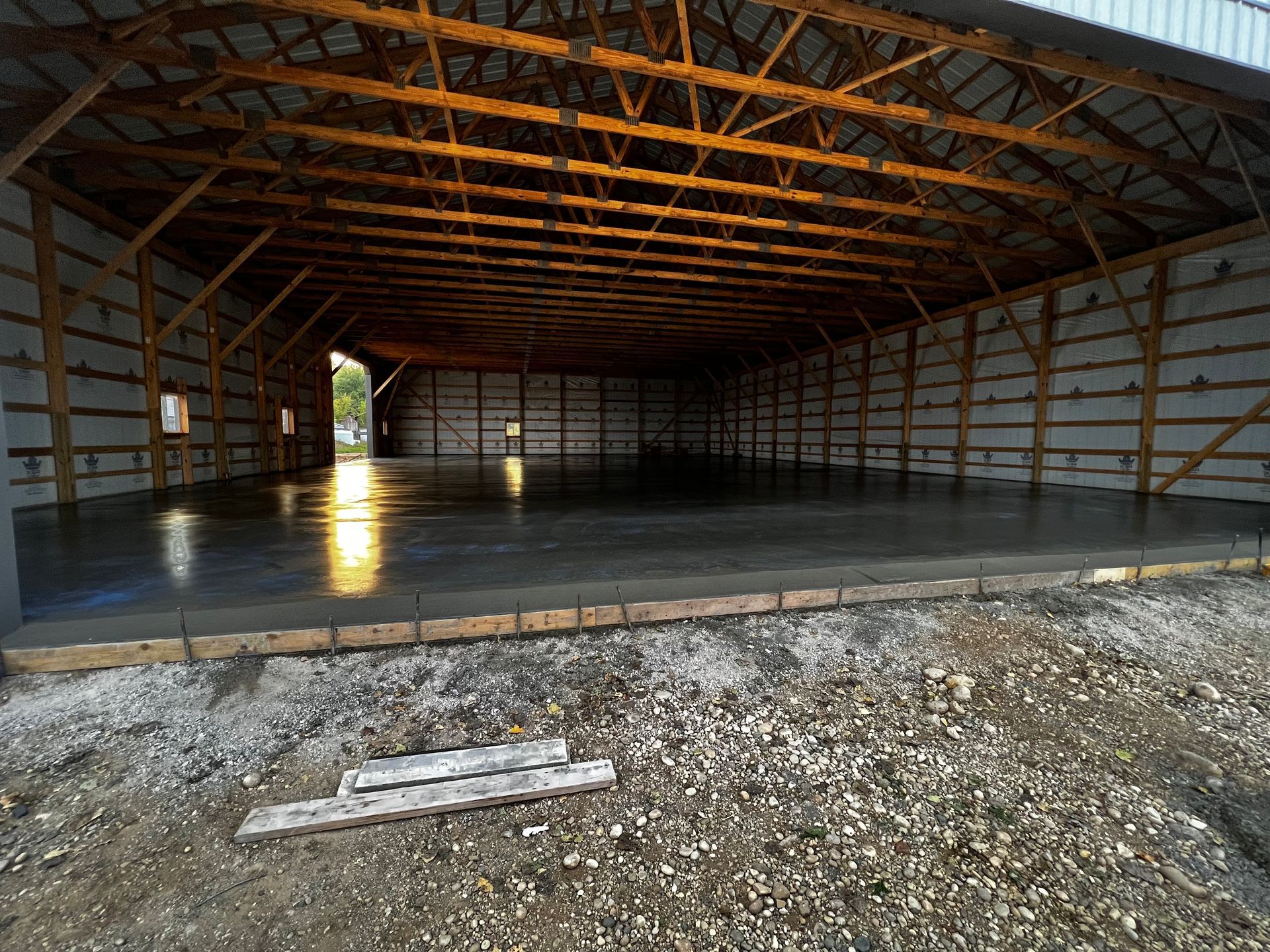 The inside of a barn with a concrete floor and wooden beams.