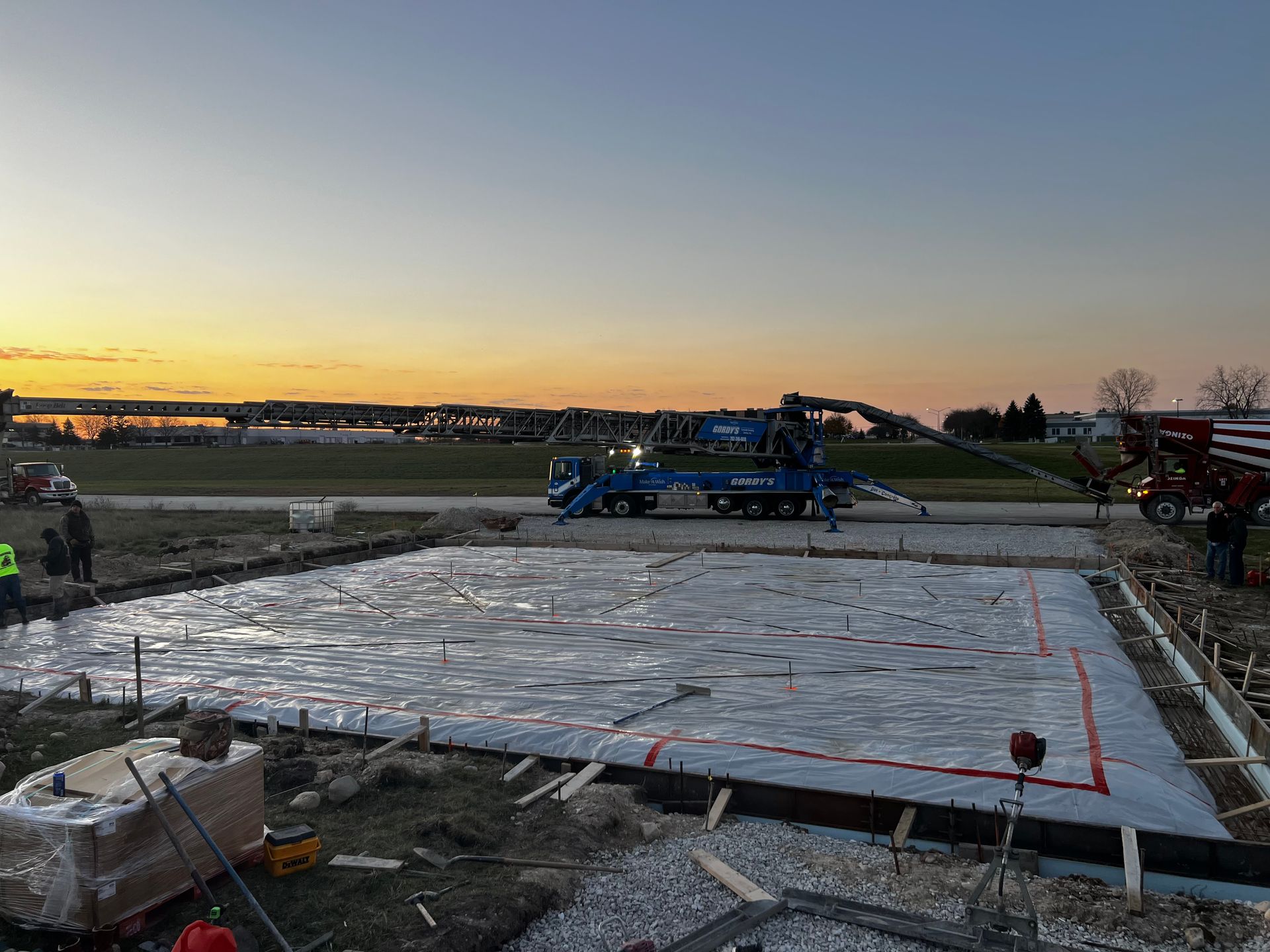 A large concrete slab is being poured on a construction site at sunset.