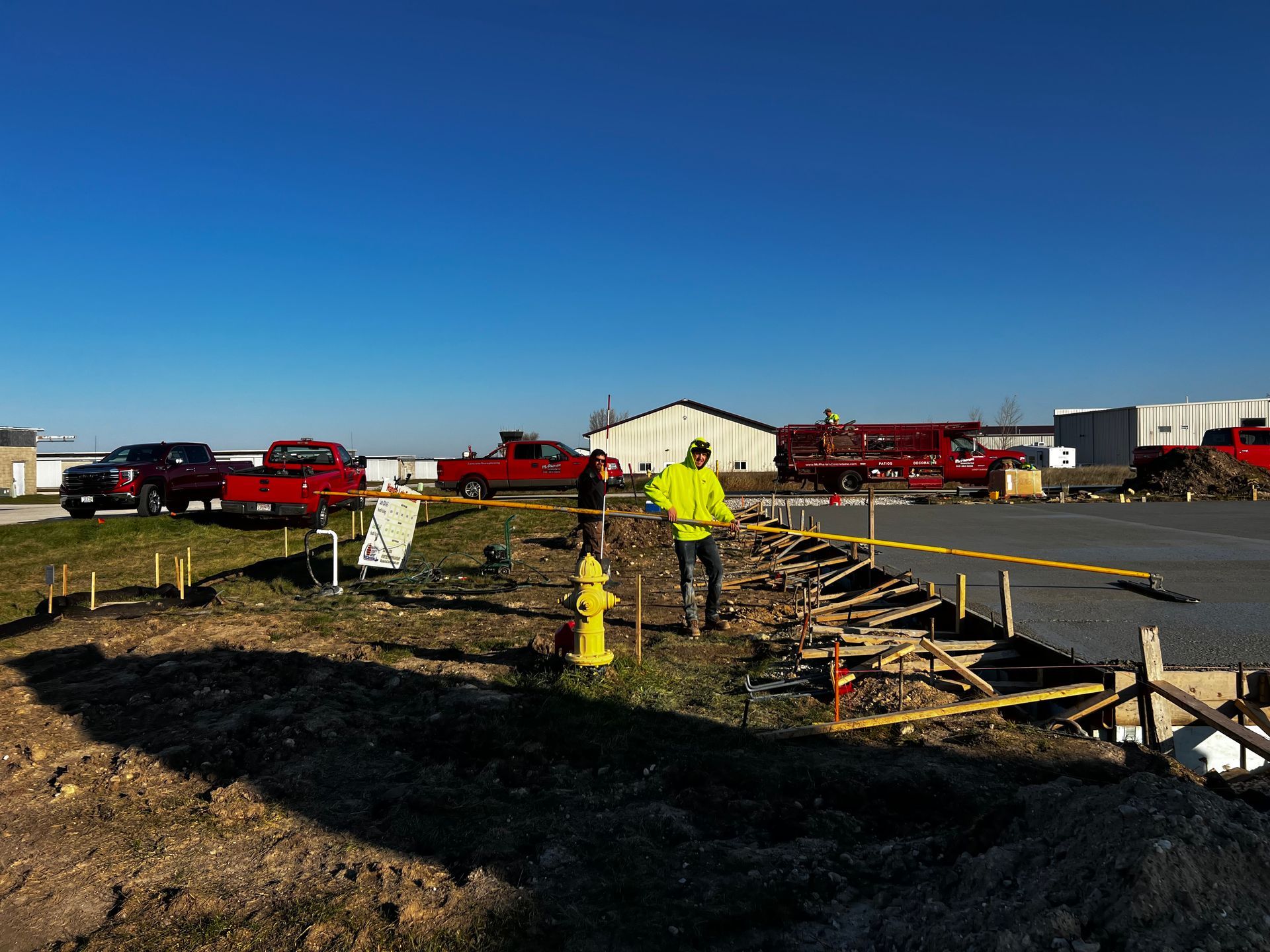 A man in a yellow jacket is standing next to a fire hydrant on a construction site.