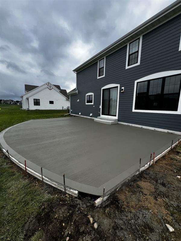Newly poured concrete patio next to a two-story gray house. Overcast sky.