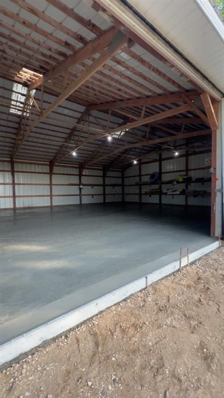 Inside of a large, empty metal building with a concrete floor, with the door open to the outside.