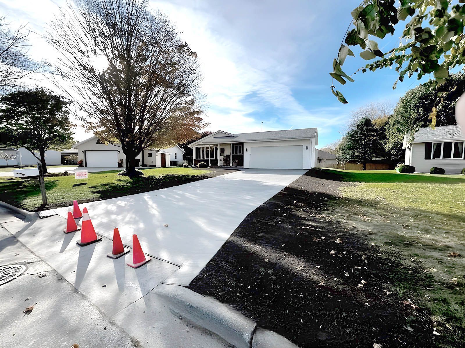 A row of orange traffic cones sit on the sidewalk in front of a house