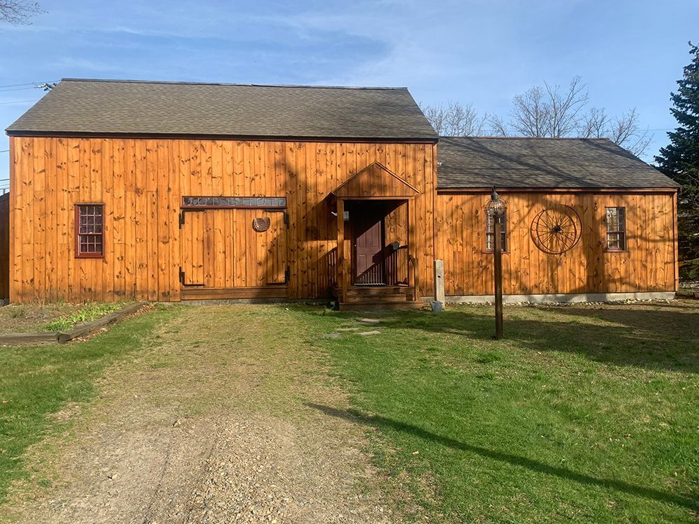 A large wooden barn is sitting in the middle of a grassy field.