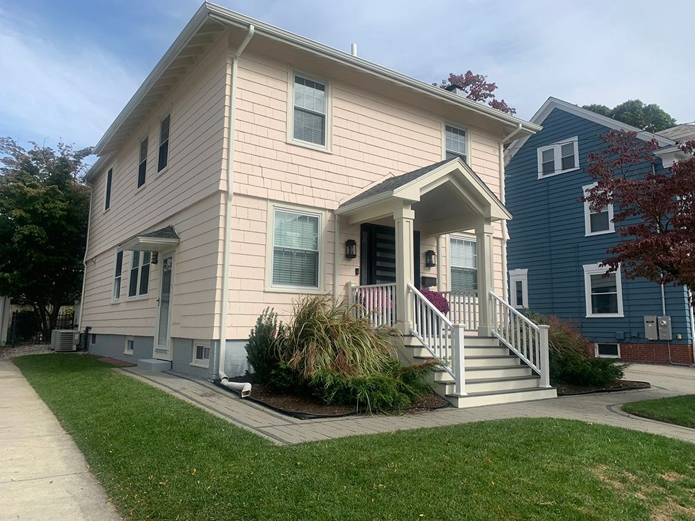 A white house with a porch and stairs next to a blue house