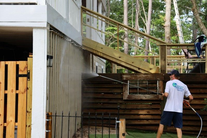 A man is cleaning a wooden fence with a high pressure washer.
