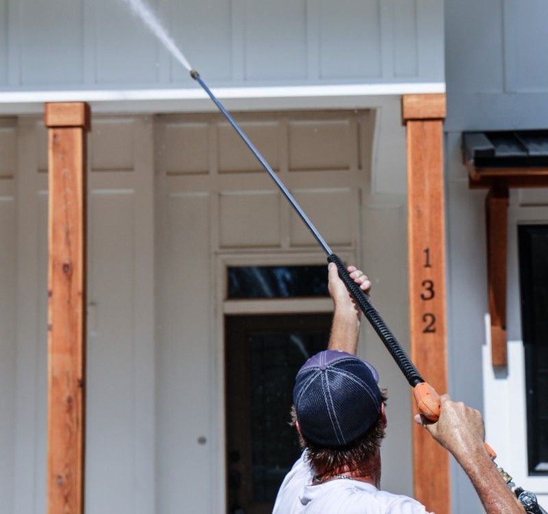 A man is using a high pressure washer to clean the outside of a house.