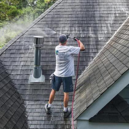 A man is cleaning the roof of a house with a pressure washer.