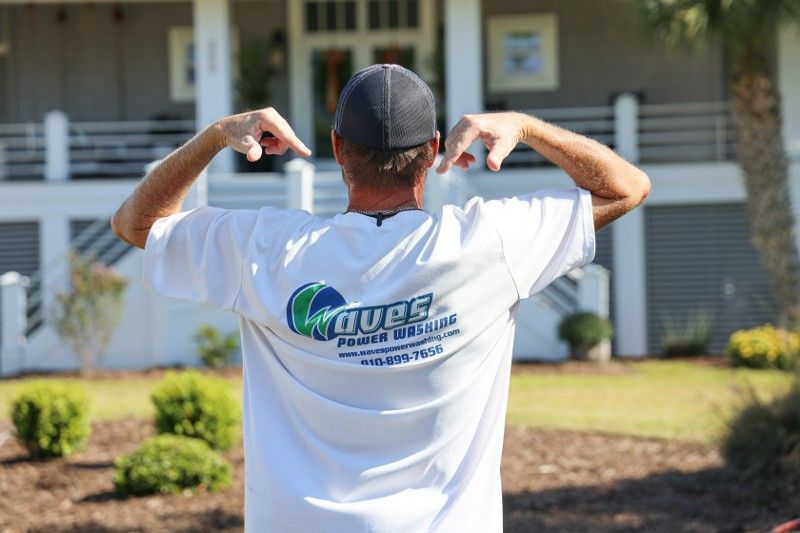 A man in a white t-shirt is standing in front of a house.