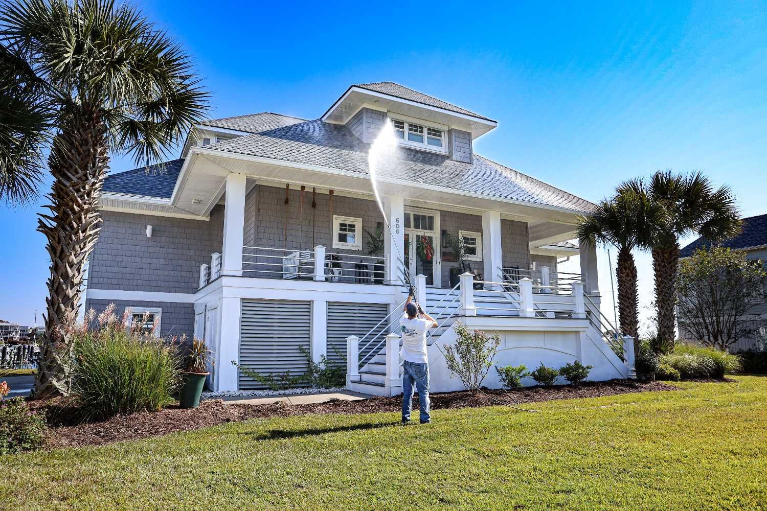 A man using a power washing cleaning equipment to a large house.