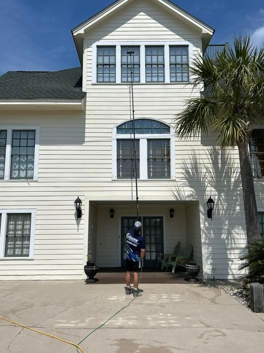 A man is cleaning the windows of a large white house.
