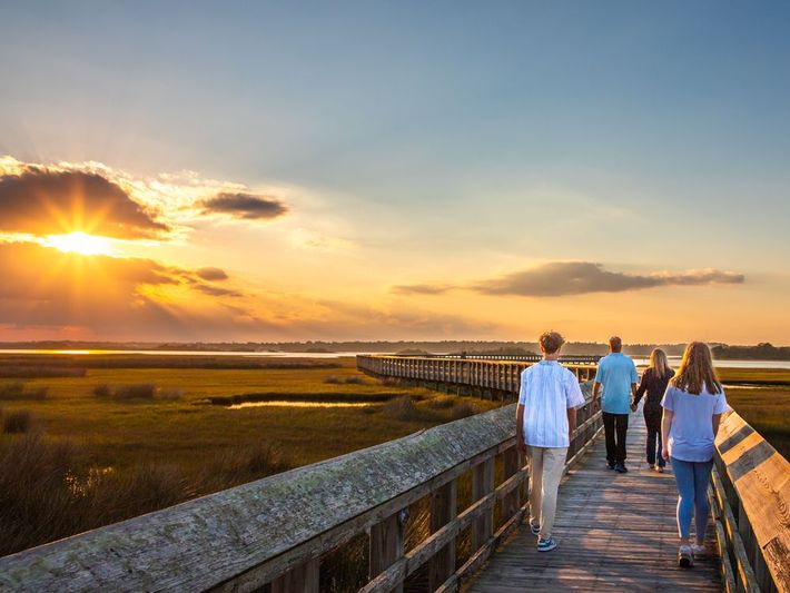 A family is walking across a wooden boardwalk at sunset.