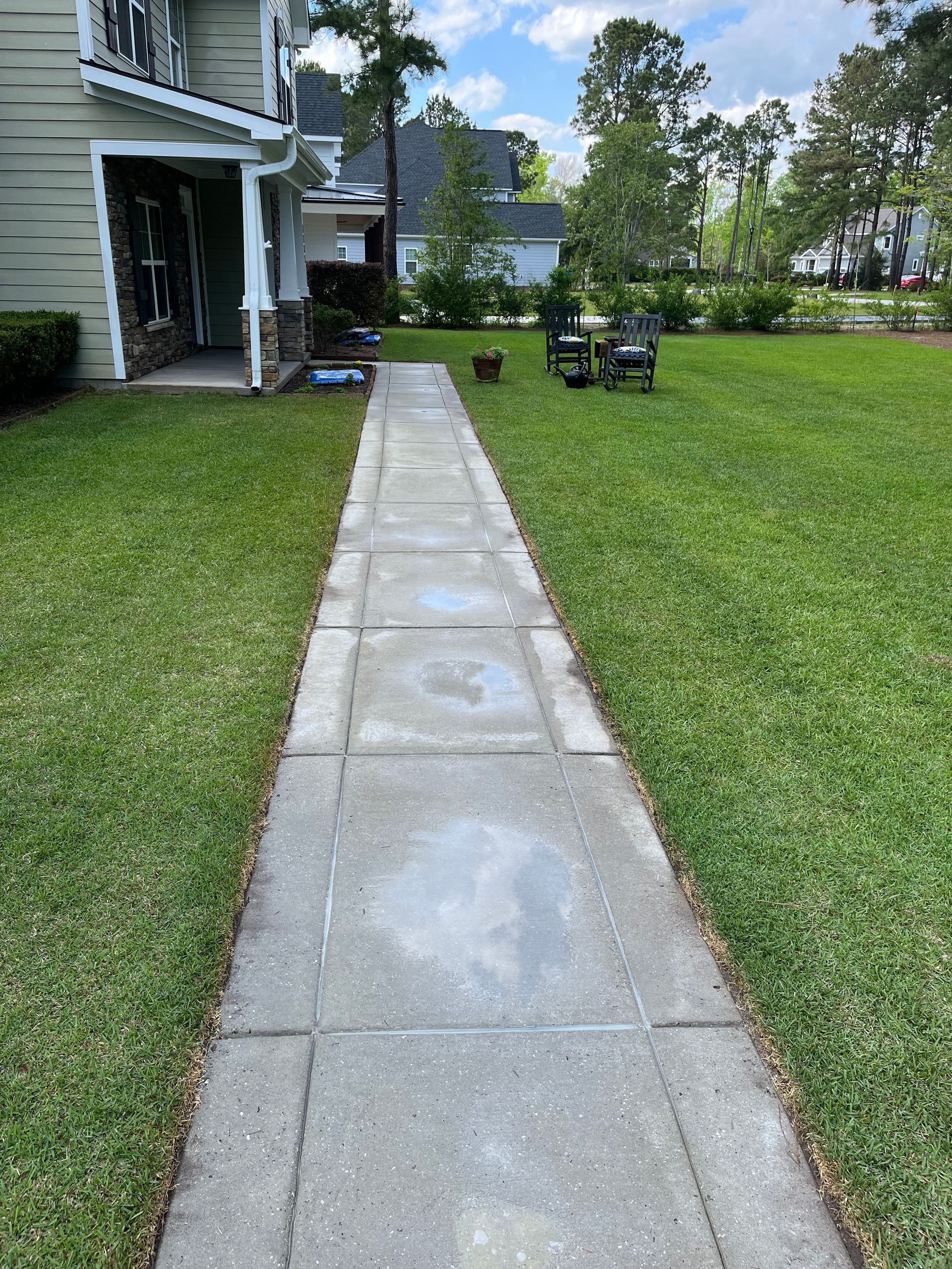 A concrete walkway leading to a house with a lush green lawn.