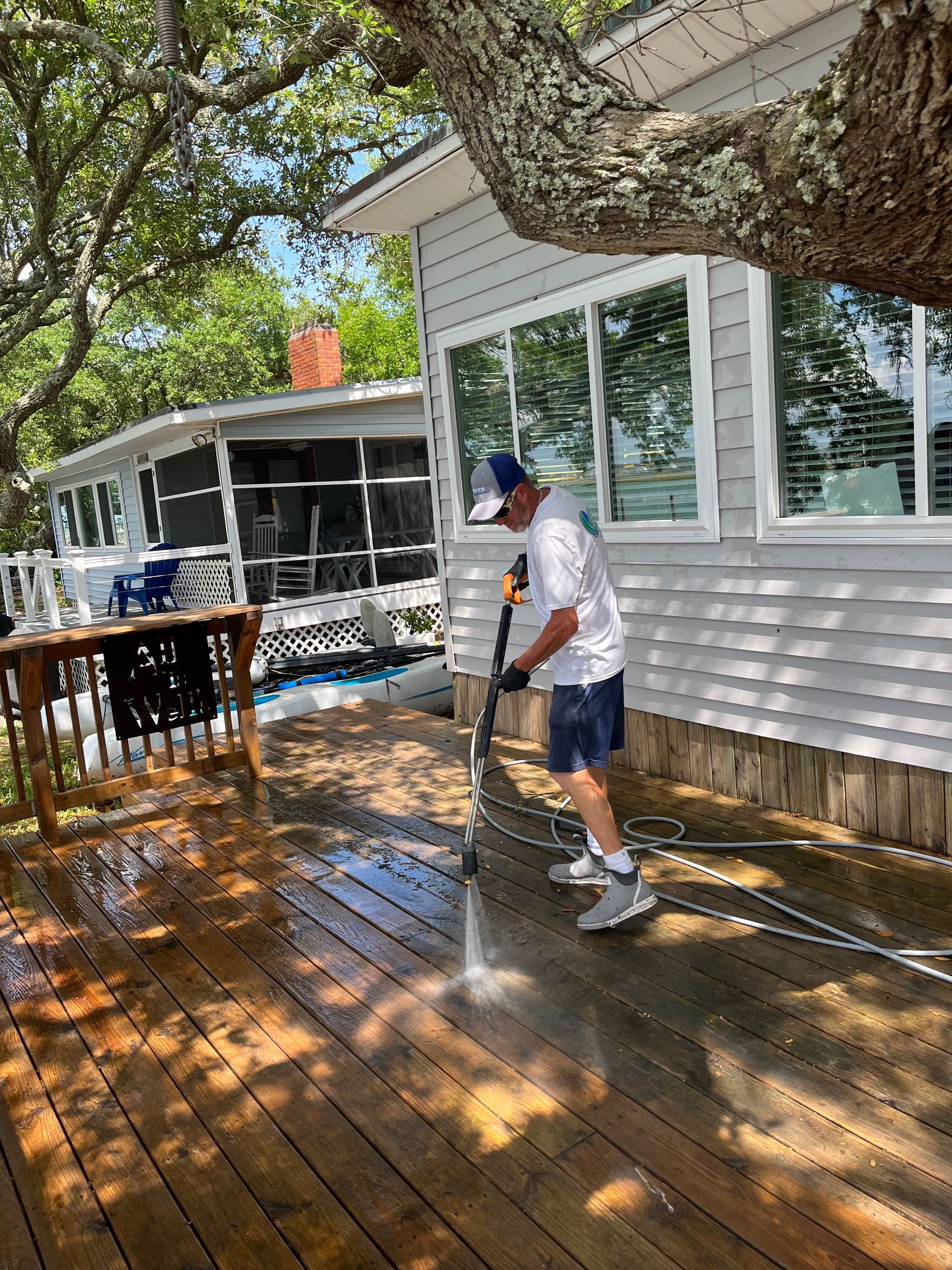 A man is cleaning a wooden deck with a pressure washer.