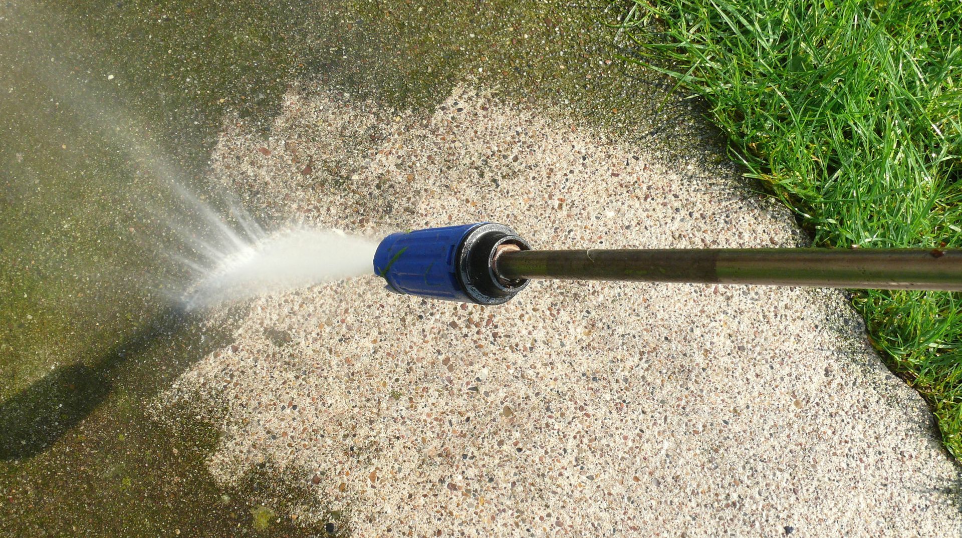 A person is using a high pressure washer to clean a sidewalk.
