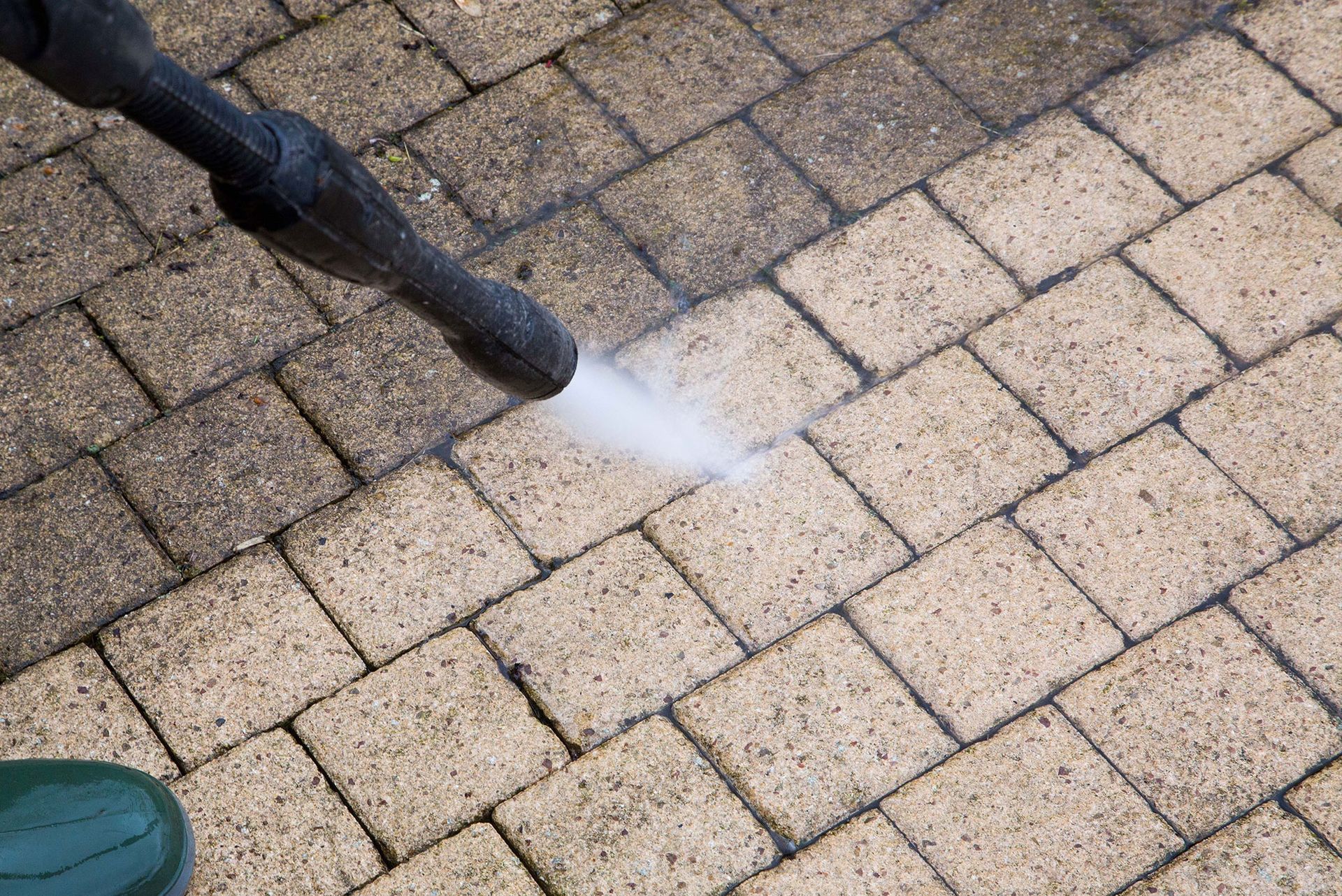 A person is cleaning a brick walkway with a high pressure washer.