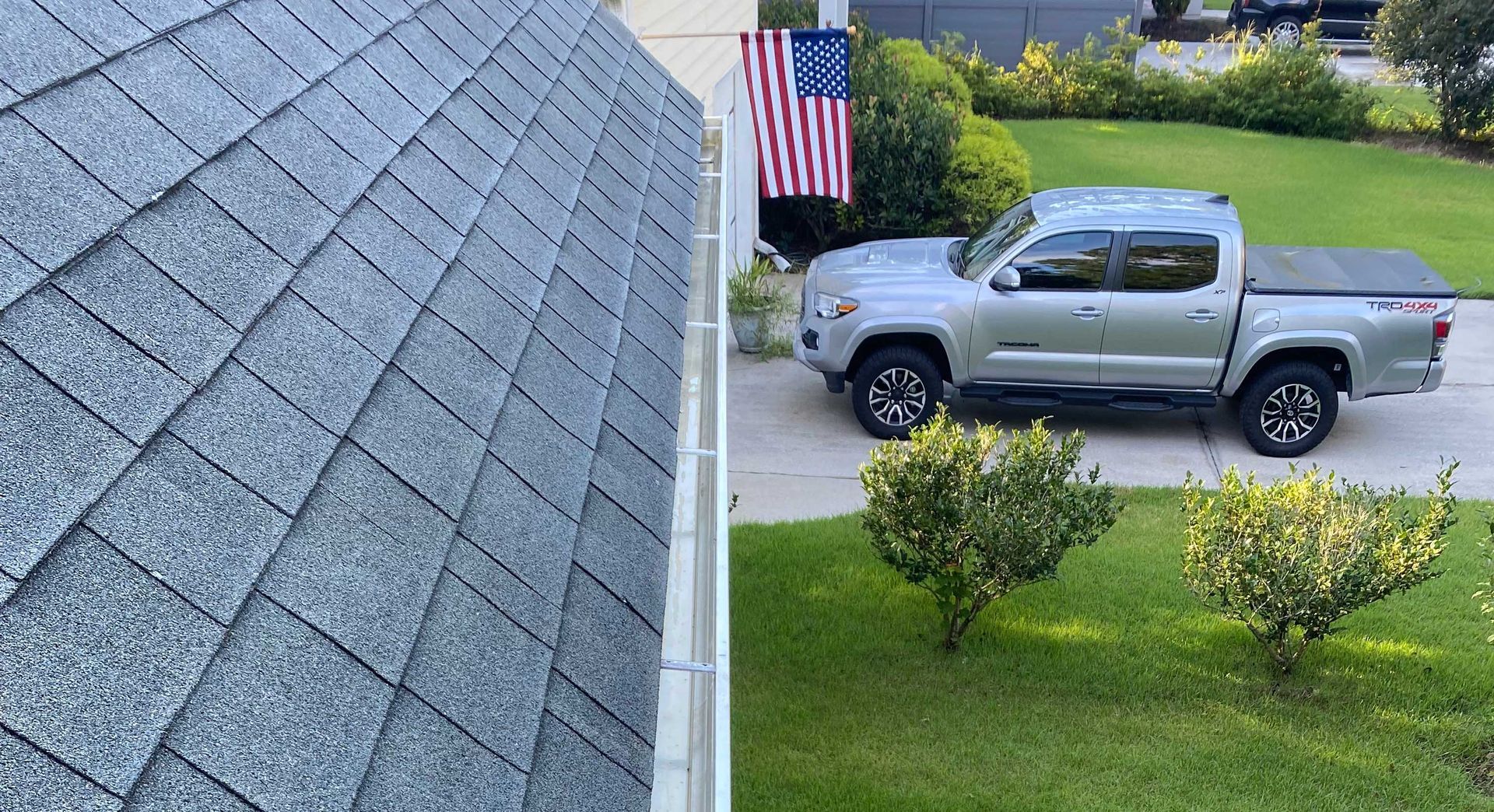 A silver truck is parked in front of a house with an american flag in the background.