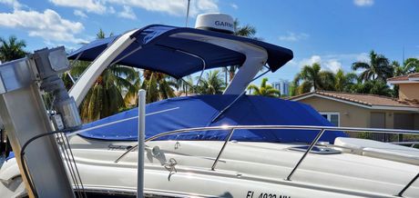 A white boat with a blue canopy is parked in front of a house.