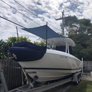 A white boat is on a trailer with a blue sail.