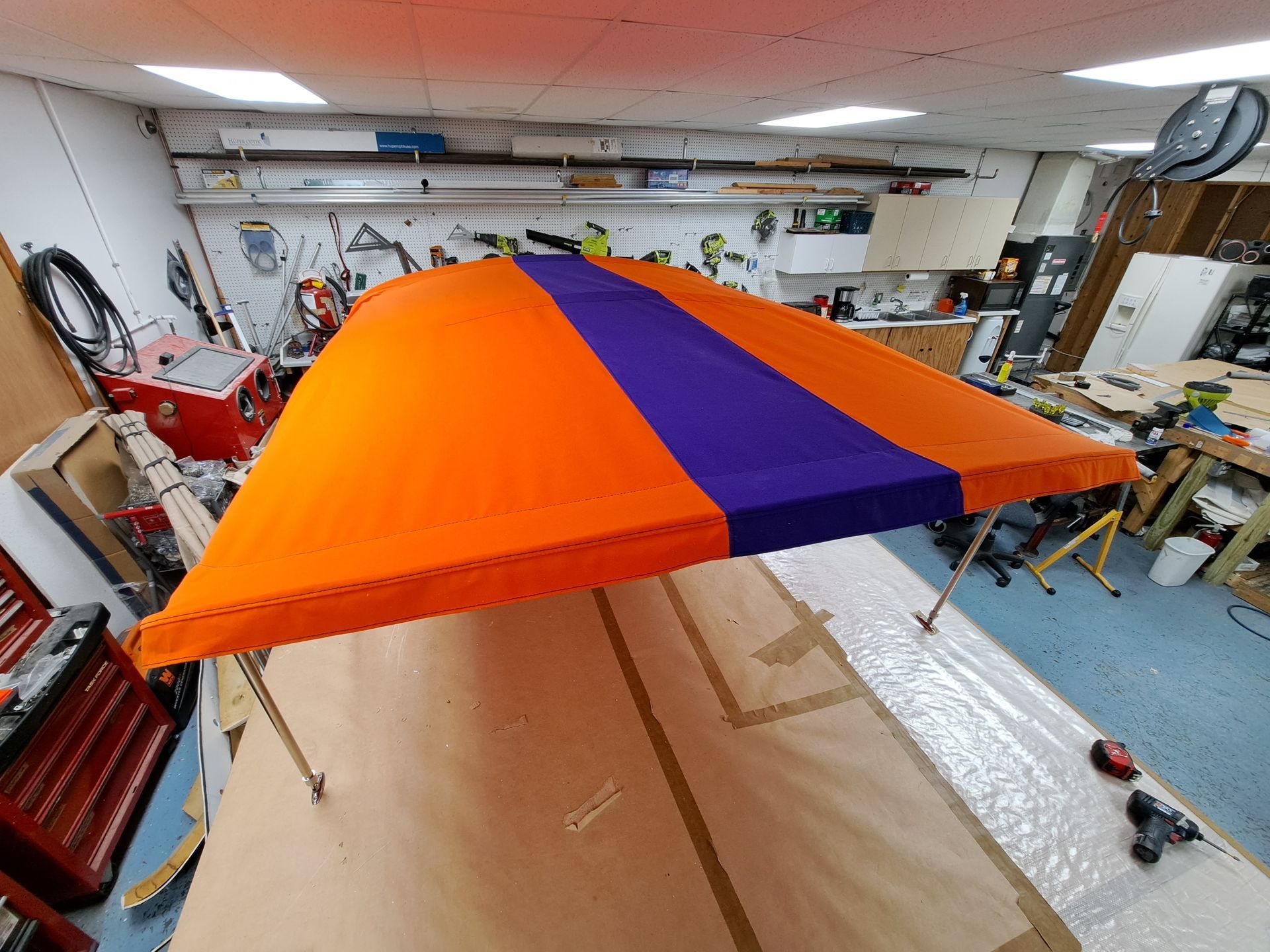 A large orange and purple umbrella is sitting on a table in a workshop.