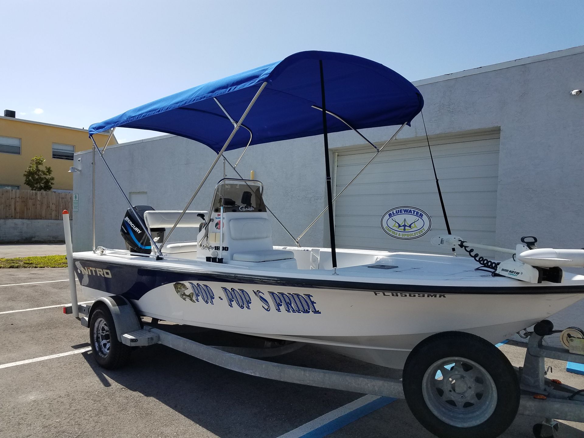A white boat with a blue canopy is parked in a parking lot
