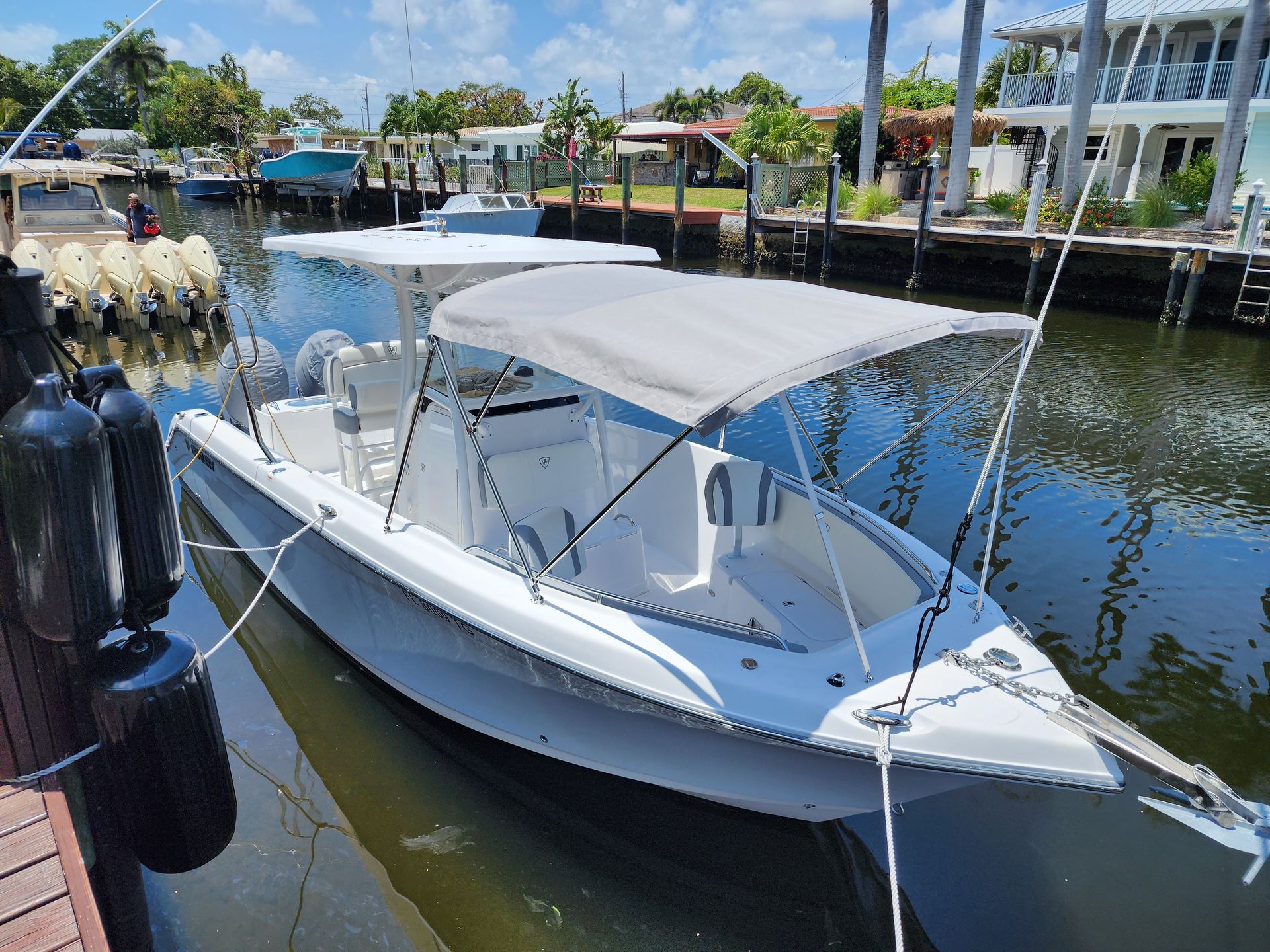 A white boat with a canopy is docked in a marina.