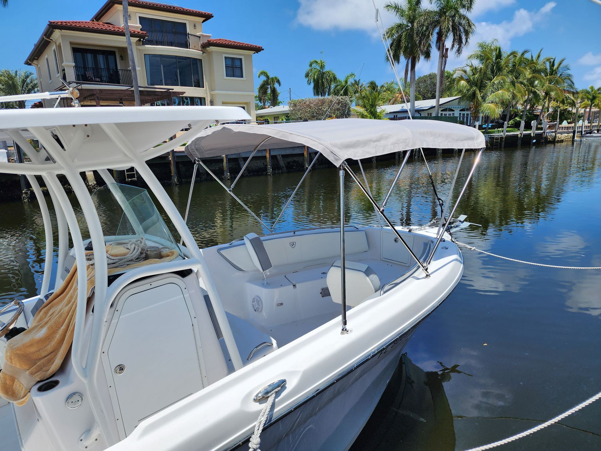 A white boat with a canopy is docked in the water near a house.
