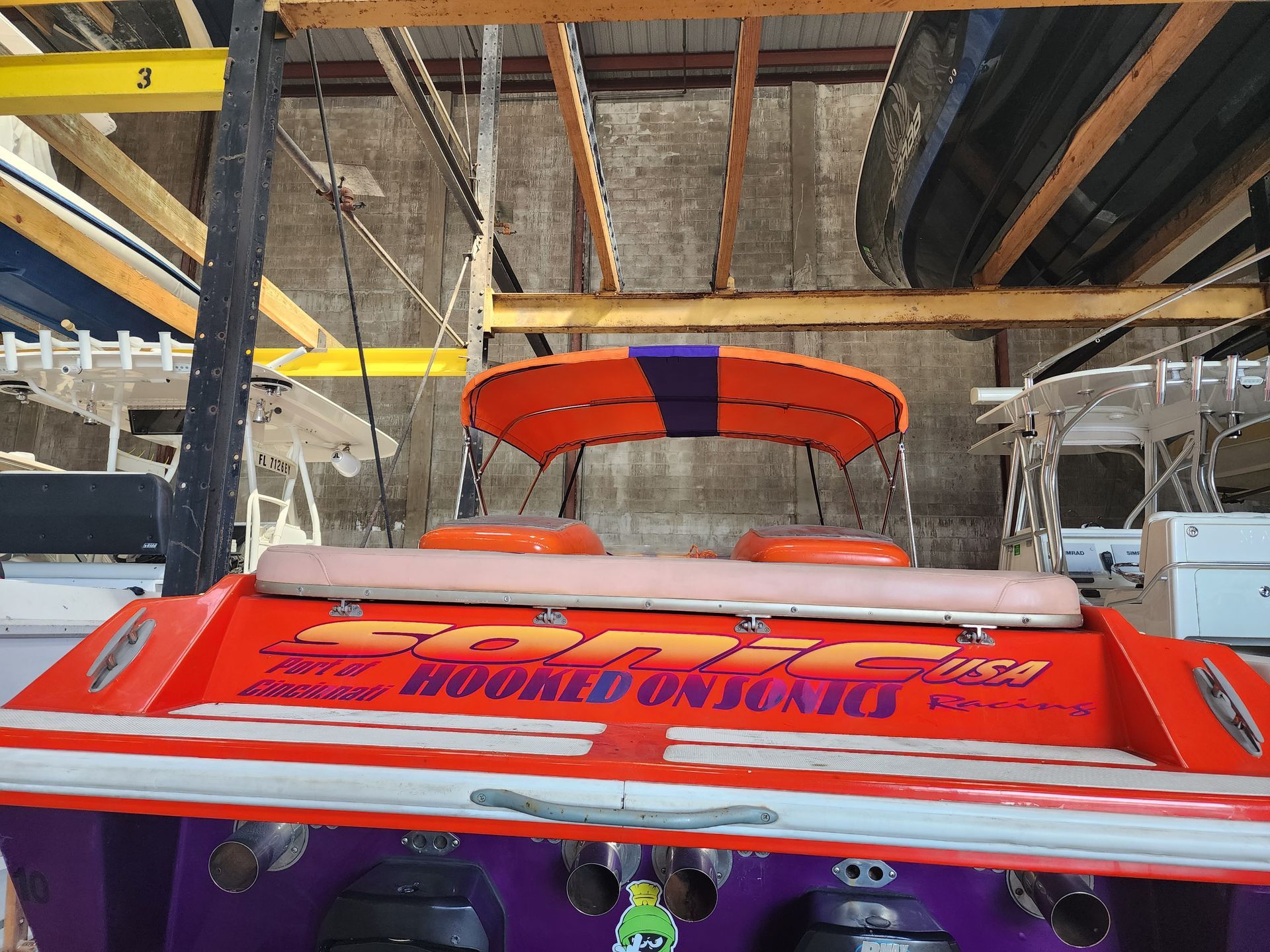 A purple and orange boat is sitting in a warehouse.