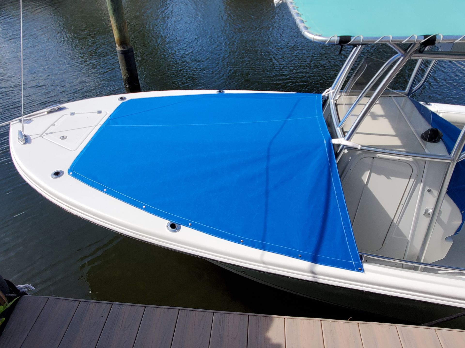 A white boat with a blue cover is docked at a dock