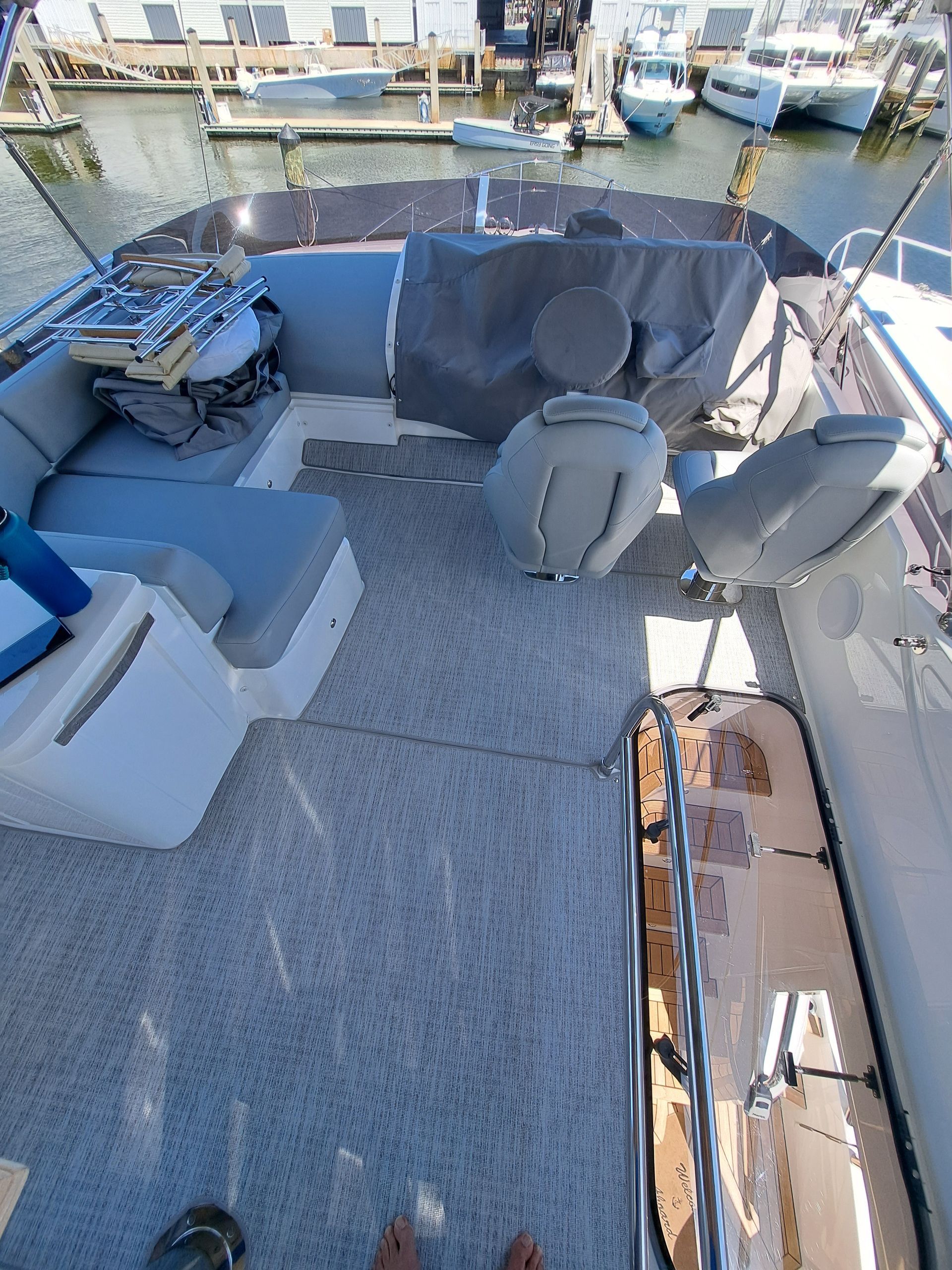 A boat with a couch and chairs on the deck is docked in a marina.