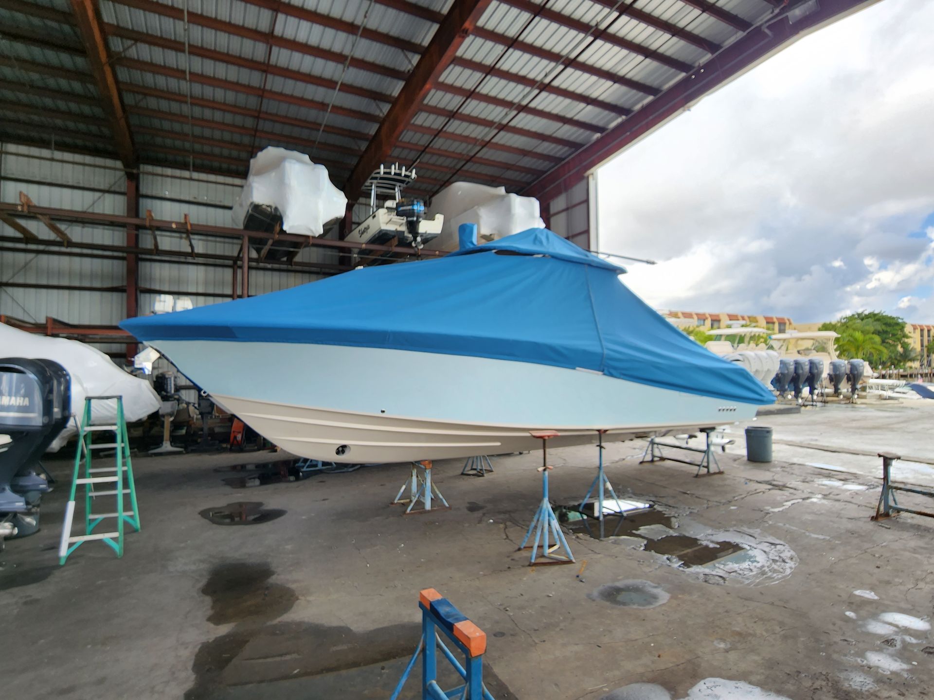 A boat is covered in a blue tarp in a warehouse.