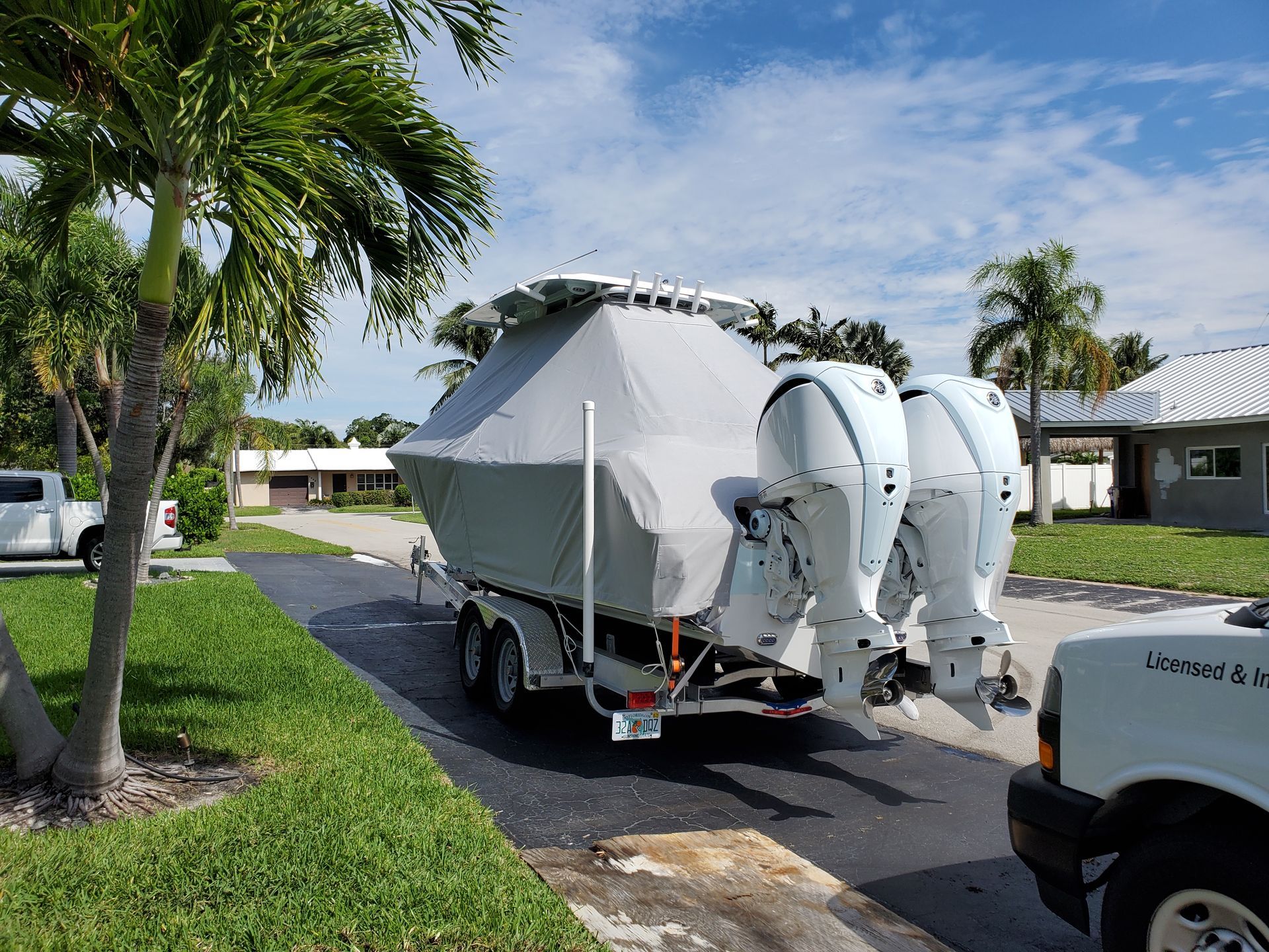 A boat on a trailer is parked on the side of the road next to a truck.