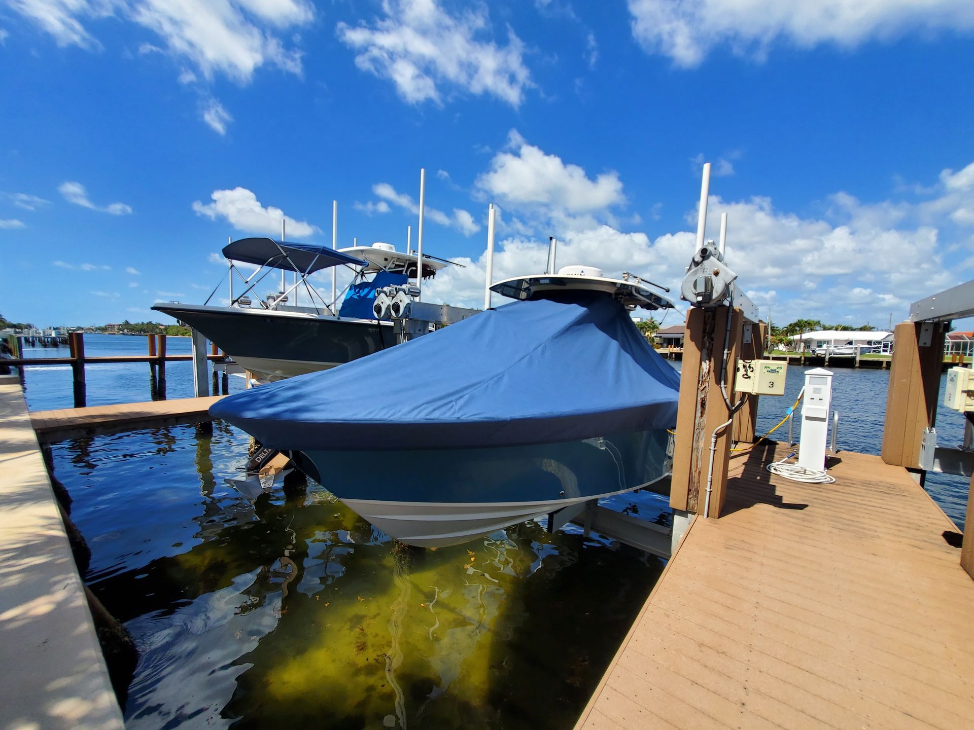 Two boats are docked at a dock with a blue cover on them.