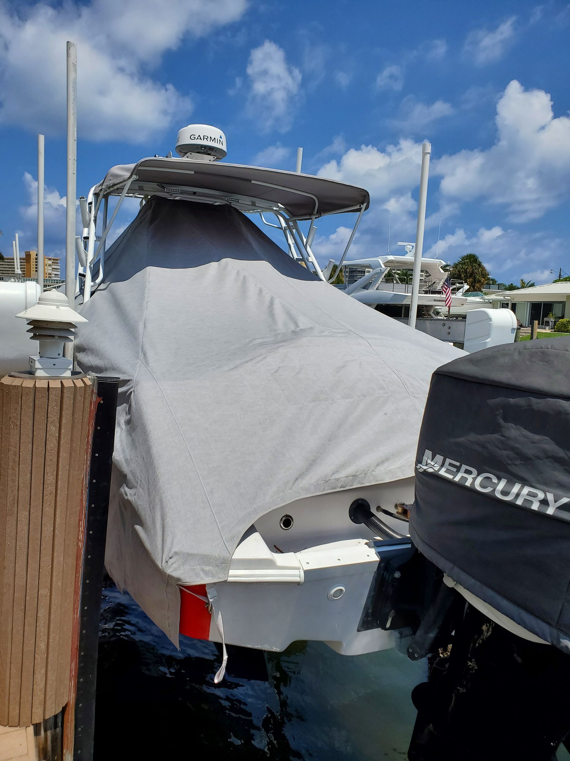 A boat with a cover on it is docked next to a mercury engine